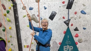 A woman is laughing as she operates a belay rope for an unseen climber