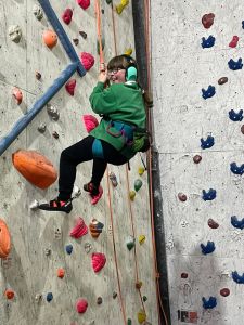 A girl with headphones and a big smile is holding onto the belay rope and bouncing down the climbing wall
