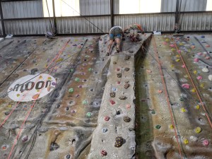 2 roped climbers are at the top of a Pillar between wide and tall climbing walls, one of which has a large "moon" logo