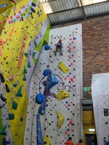 A boy in harness and helmet is at the top of a high climbing wall