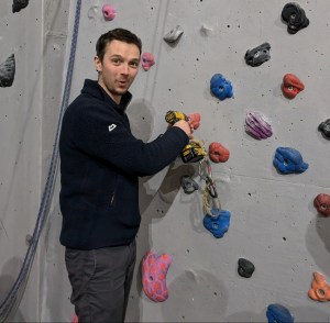 A man attaches a climbing hold to the wall using a cordless drill