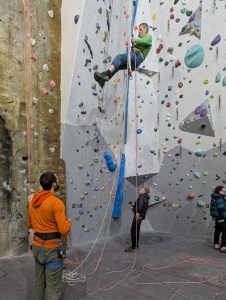 A climber lowers from roof beside a hanging rope system with two roped climbers below