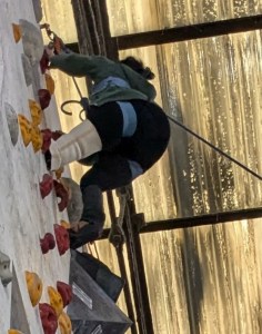 A climber with a limb difference grasps a hold at the top of a wall and swings up to mounting point